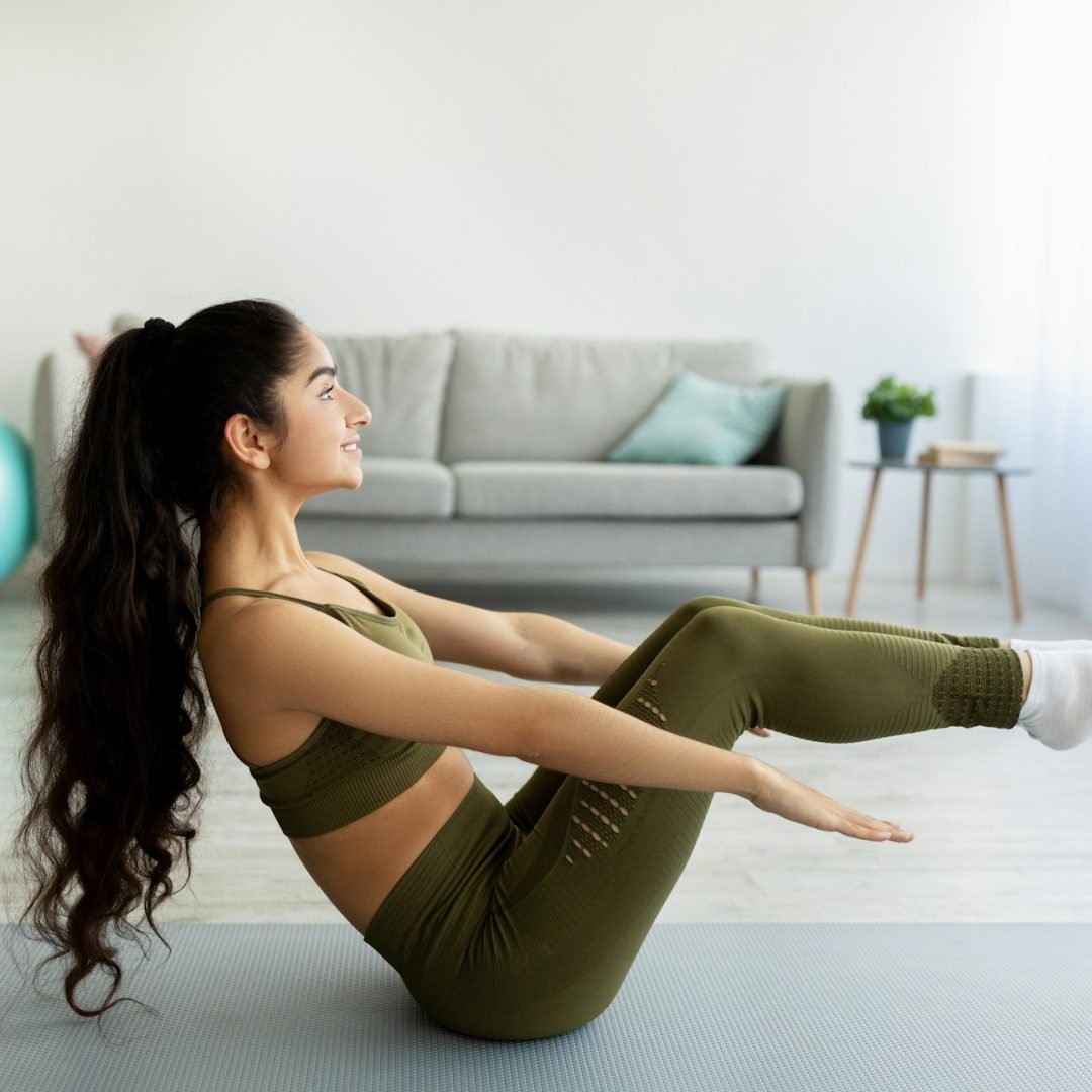 Athletic Indian woman doing yoga, performing boat pose during her domestic workout at home